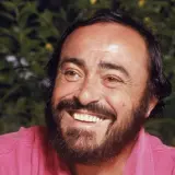 Uśmiechnięty Luciano Pavarotti w różowej koszuli, z charakterystyczną brodą i bujnymi włosami.