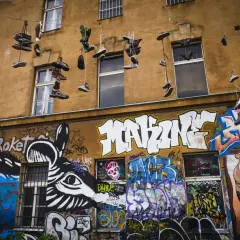 Instalacja artystyczna na fasadzie kamienicy: wiszące buty i kolorowe graffiti.