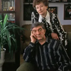 Jerzy Trela z żoną, w domu, wśród roślin. W tle widać zdjęcia, jakby wspomnienia o jego dzieciach.