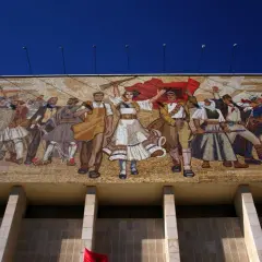 Socrealizm co to? Wielki mozaikowy mural przedstawiający ludzi w strojach ludowych i wojskowych, z flagami i bronią, symbolizujący walkę i jedność.