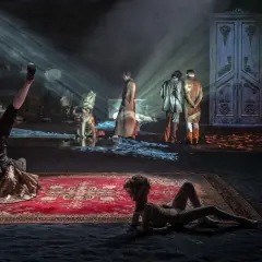 Scenograf tworzy surrealistyczny świat. Na scenie akrobata, dwie postacie w strojach z epoki i wielkie drzwi.