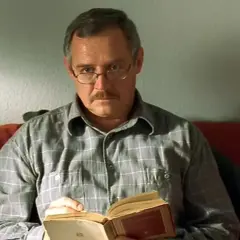 Mężczyzna w okularach i kratowanej koszuli czyta książkę. To Marek Kondrat, jeden z aktorów z obsady "Dnia świra".