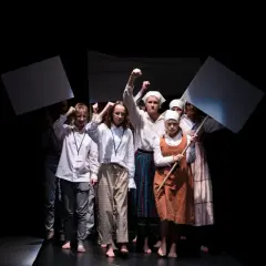 Młoda grupa teatralna z transparentami wznosi pięści. Występ na czarnym tle.