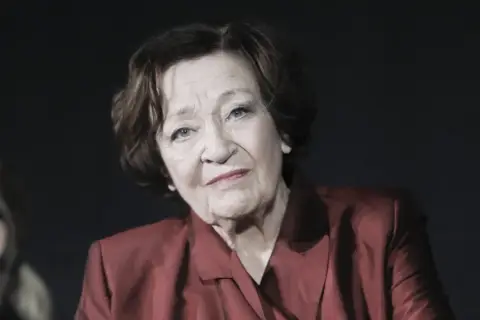 Portret Ewy Dałkowskiej, aktorki, której wiek dodaje jej charyzmy. W czerwonej marynarce patrzy zamyślona.