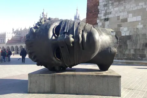 Gigantyczna, metalowa głowa, dzieło polskiego rzeźbiarza, leży na cokole na krakowskim Rynku.