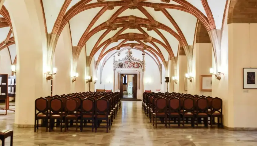 Wnętrze sali z rzędami krzeseł i ozdobnym sklepieniem.