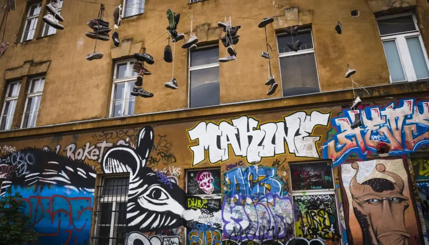 Instalacja artystyczna na fasadzie kamienicy: wiszące buty i kolorowe graffiti.