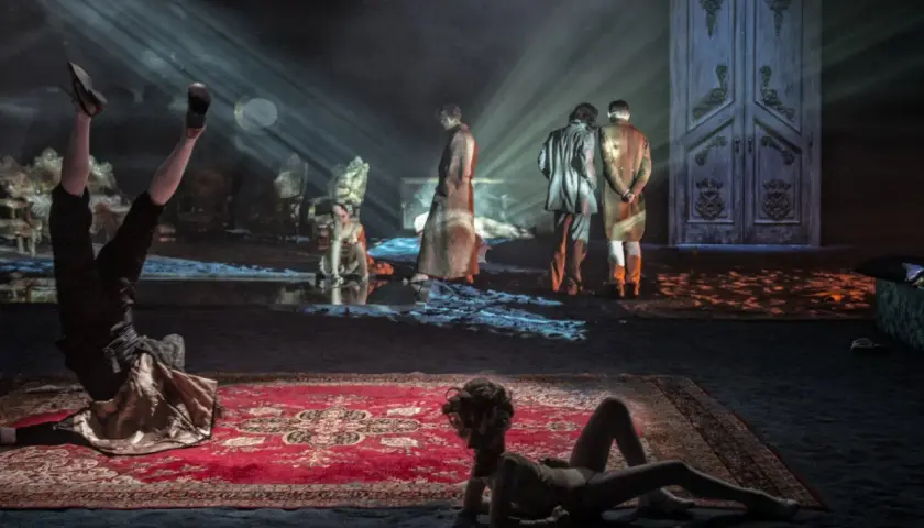 Scenograf tworzy surrealistyczny świat. Na scenie akrobata, dwie postacie w strojach z epoki i wielkie drzwi.