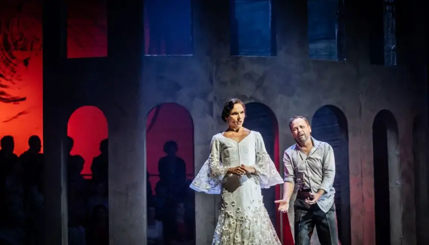 Carmen w białej sukni i mężczyzna na scenie operowej. Tło z łukami i czerwonymi światłami.