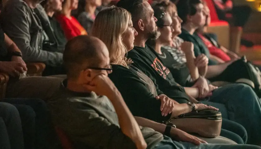 Widownia w teatrze siedząca w rzędach, skupiona na spektaklu.