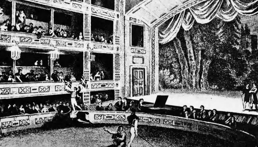 Widownia wypełnia wielopoziomowe loże, a na arenie trwa spektakl. To scena z życia teatru średniowiecznego, pełna widzów i aktorów.
