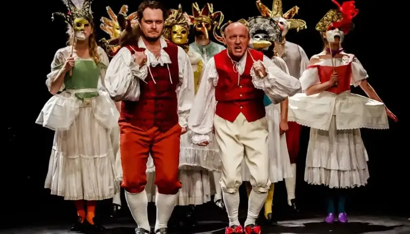 Aktorzy Teatru Ateneum w barwnych strojach i maskach, przygotowują się do wejścia na scenę.