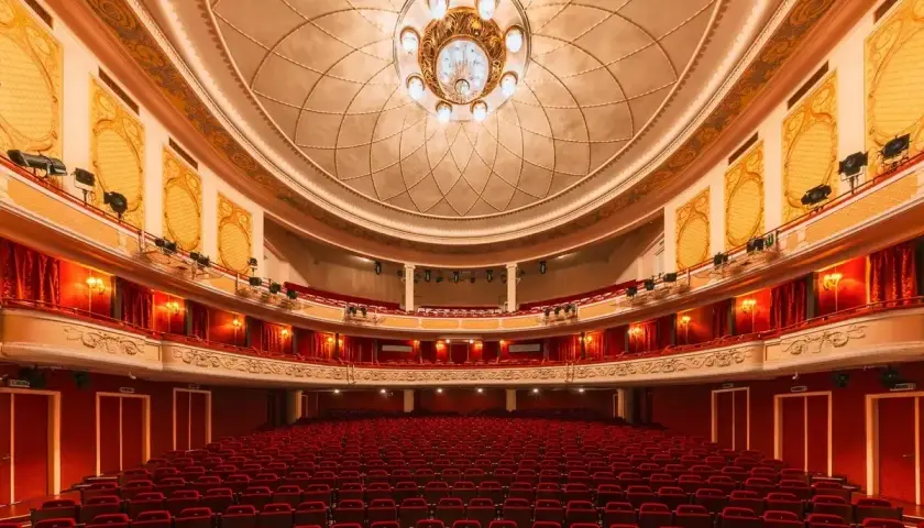 Wnętrze teatru z czerwonymi fotelami i bogato zdobionym sufitem. Czekamy na wspaniały występ.
