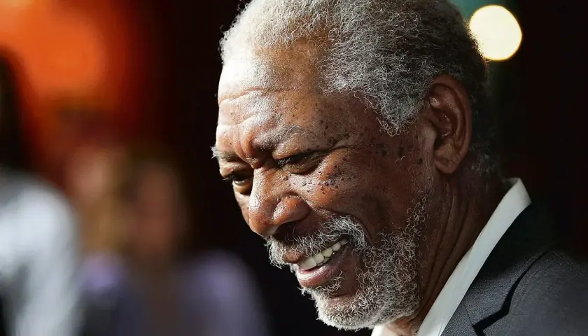 Uśmiechnięty aktor murzyn, Morgan Freeman, z siwą brodą i kręconymi włosami, w garniturze.