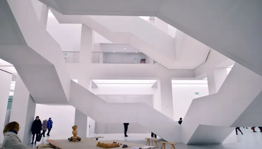 Nowoczesne muzeum sztuki z białymi, geometrycznymi schodami i kilkoma zwiedzającymi.