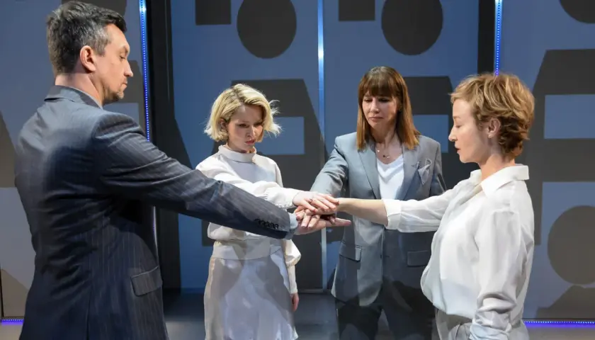Cztery osoby łączą dłonie w geście jedności. To scena z nienasyceni spektakl, gdzie wspólnie budują coś ważnego.