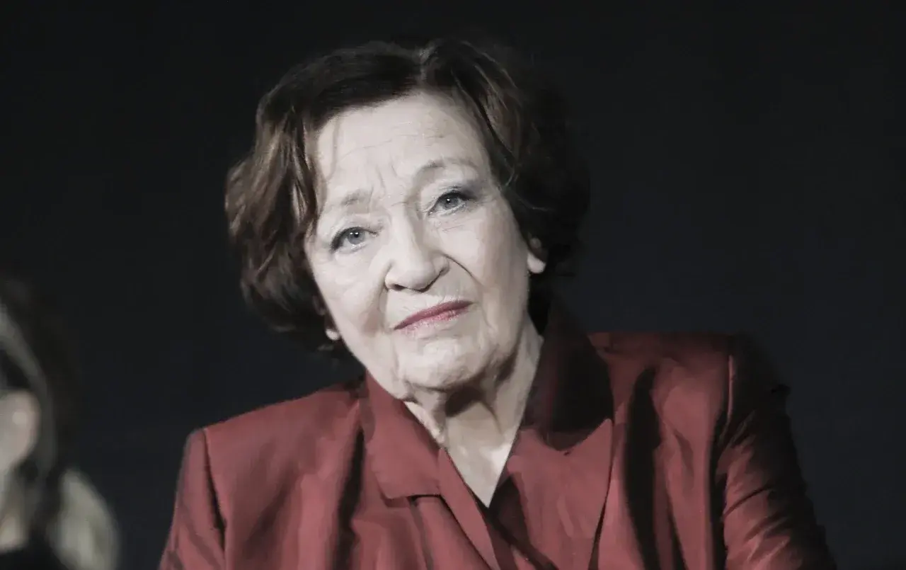 Portret Ewy Dałkowskiej, aktorki, której wiek dodaje jej charyzmy. W czerwonej marynarce patrzy zamyślona.