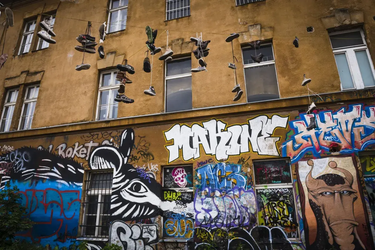 Instalacja artystyczna na fasadzie kamienicy: wiszące buty i kolorowe graffiti.