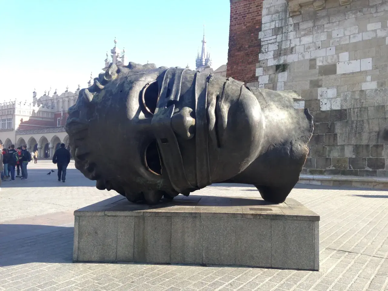Gigantyczna, metalowa głowa, dzieło polskiego rzeźbiarza, leży na cokole na krakowskim Rynku.