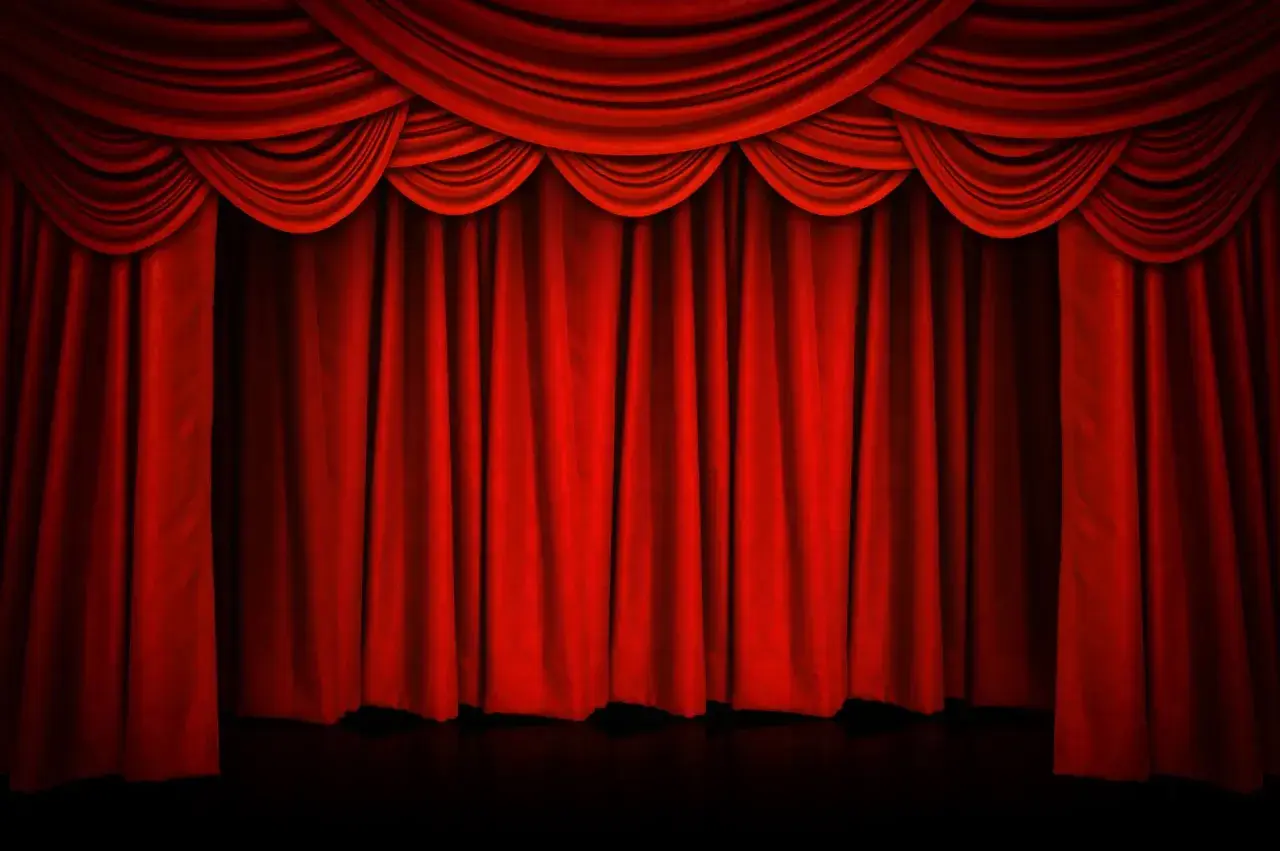 Czerwona, teatralna kurtyna w teatrze, z bogatymi drapowaniami u góry, gotowa do odsłonięcia sceny.