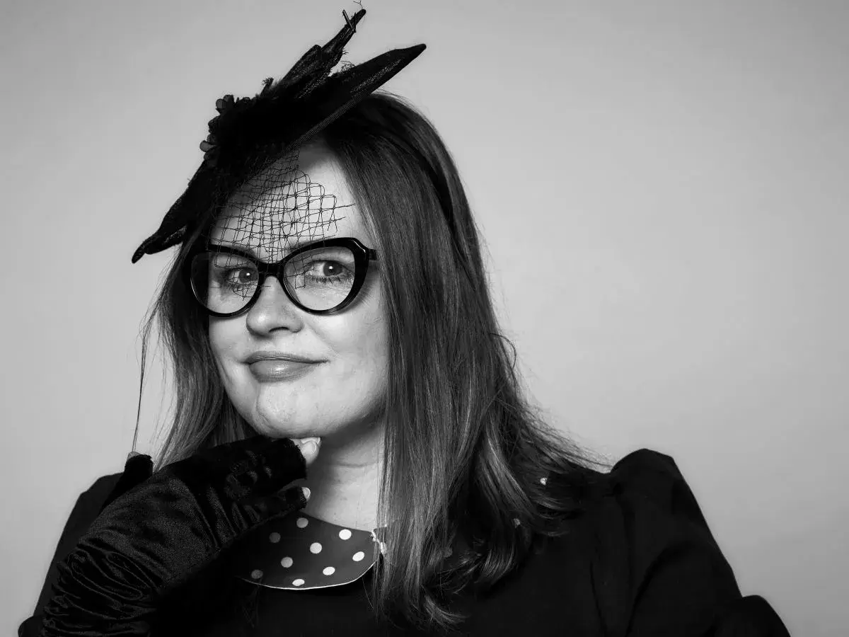 Joanna aktorka w stylowym kapeluszu i okularach, z dłonią na podbródku, gotowa na wielką rolę.