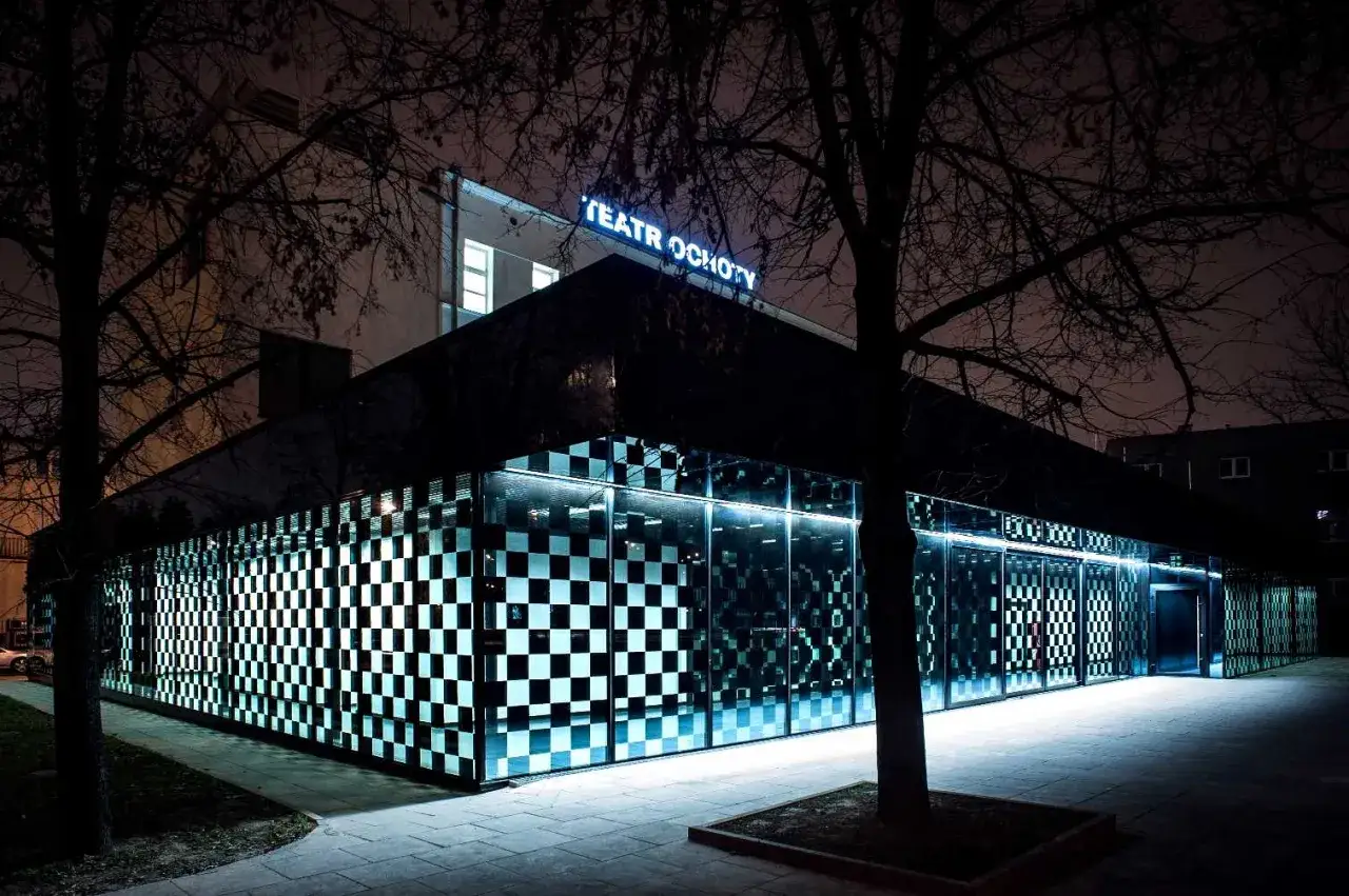 Teatr Ochoty nocą, z neonowym napisem i szachownicową fasadą. Warto sprawdzić, ile jest teatrów w Warszawie, by docenić takie perełki.
