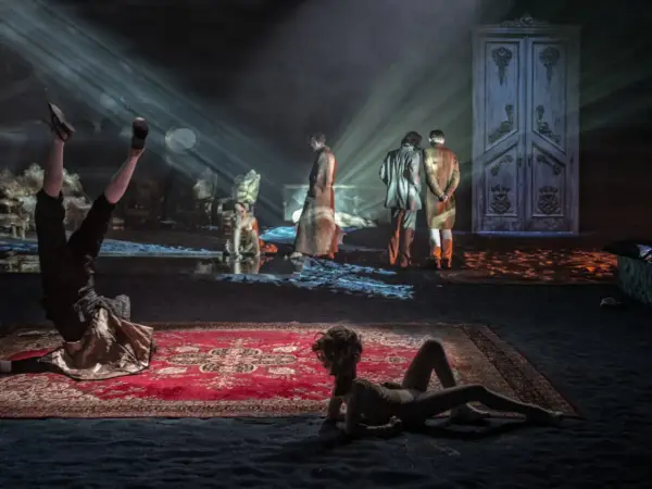 Scenograf tworzy surrealistyczny świat. Na scenie akrobata, dwie postacie w strojach z epoki i wielkie drzwi.