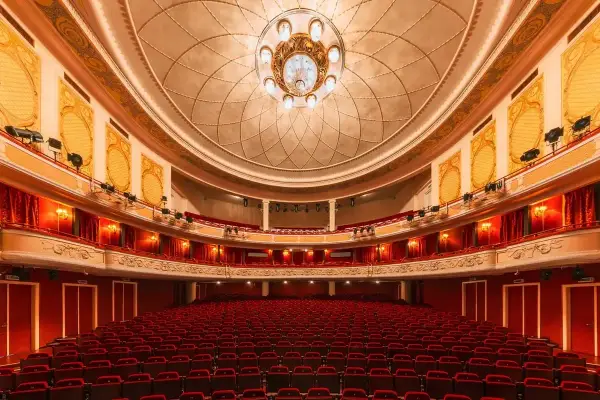 Wnętrze teatru z czerwonymi fotelami i bogato zdobionym sufitem. Czekamy na wspaniały występ.